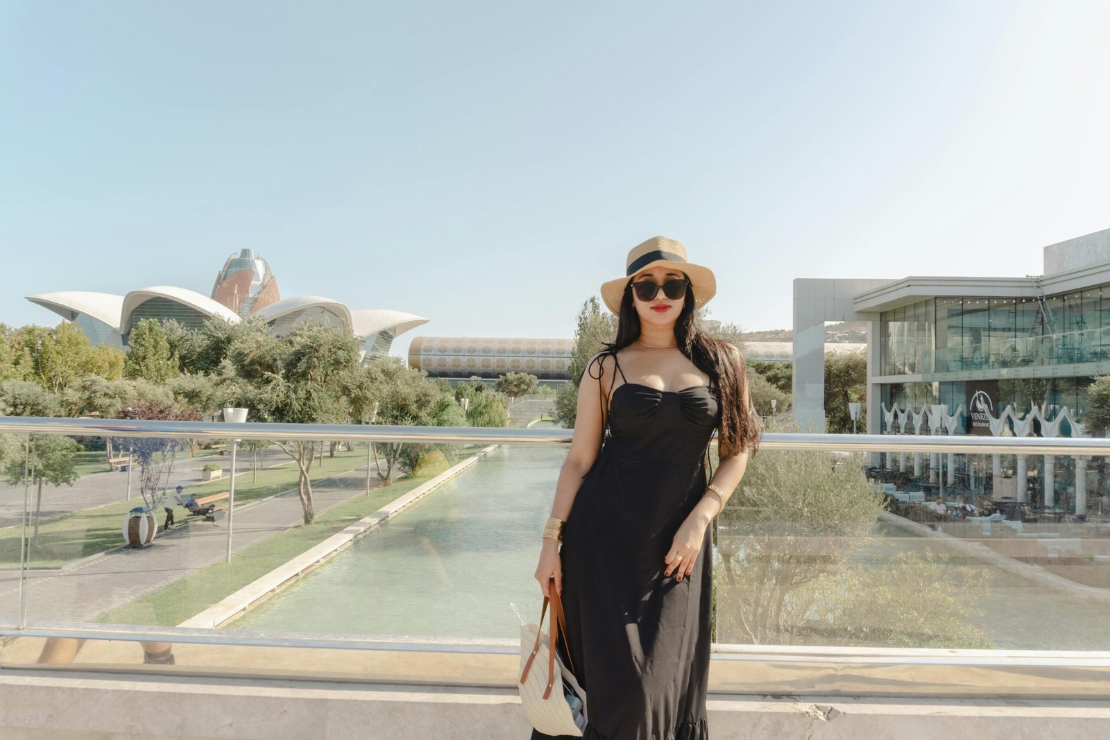 Young and beautiful female traveler wearing a stylish dress and summer hat enjoys evening ambience at the Baku Boulevard. Baku, Azerbaijan. 18.08.2025.