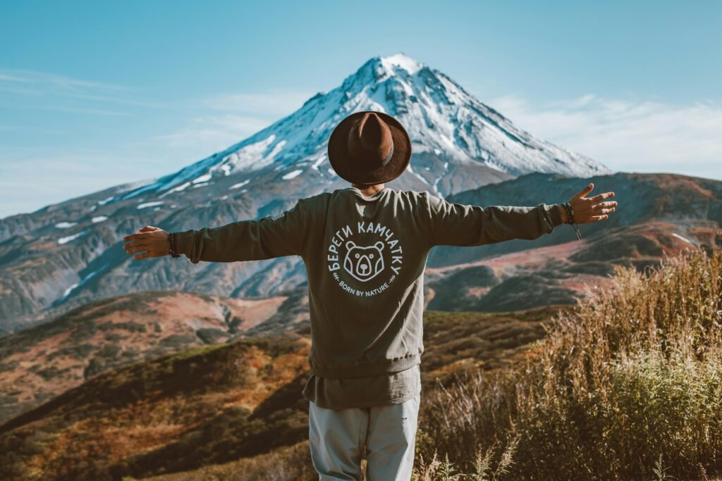 Man with outstretched arms overlooking Kamchatka's scenic volcanic landscape.