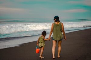 A mother and daughter walk hand in hand on a scenic beach, enjoying a serene day by the ocean.